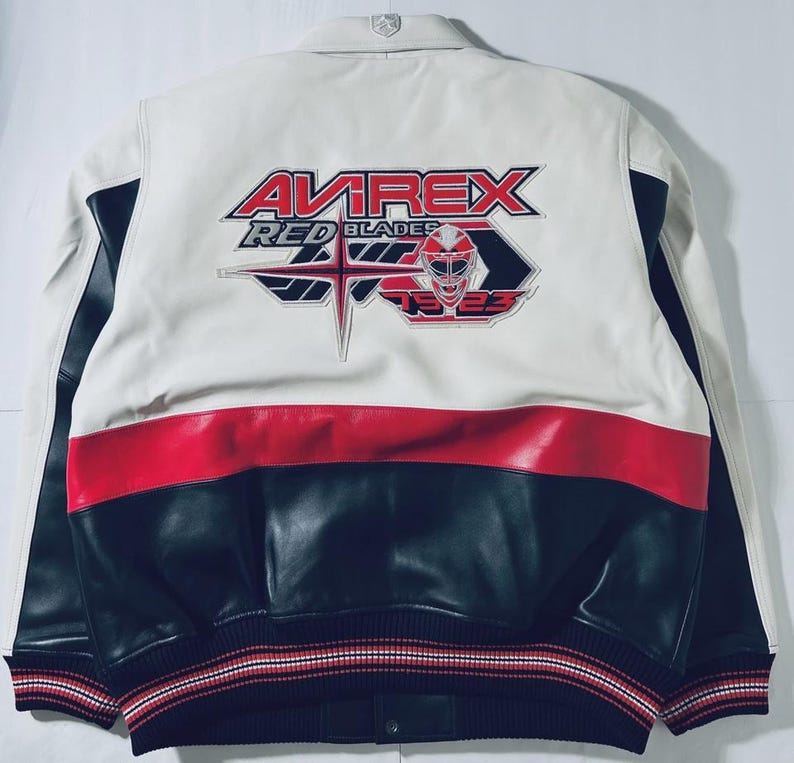 Puede incluir: Chaqueta de cuero blanca, roja y negra con el texto "AVIREX RED BLADES 1923" en la espalda. La chaqueta tiene un dise&ntilde;o tipo bomber con dobladillo y pu&ntilde;os acanalados. El dise&ntilde;o es deportivo y cl&aacute;sico.