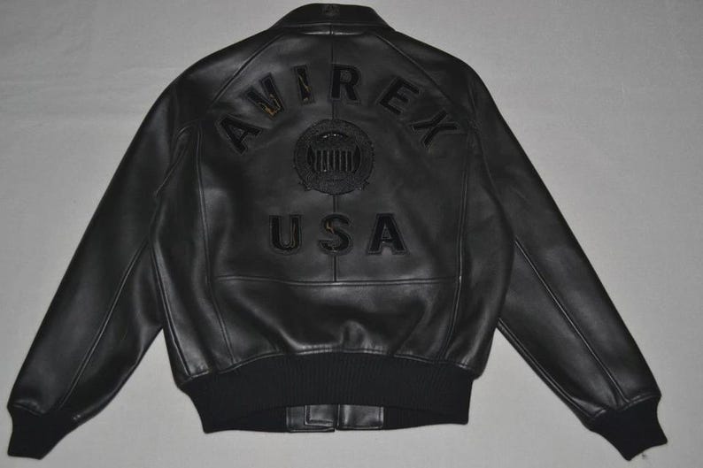 May include: Black leather jacket with the text "AVIREX USA" on the back. The jacket has a ribbed hem and cuffs, and a classic bomber jacket design. The jacket is a size large.
