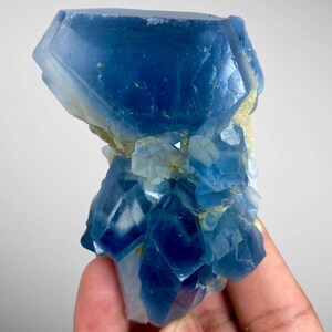 May include: A cluster of blue crystals with a complex, geometric structure. The crystals vary in shades of blue, from deep indigo to lighter, translucent hues. The mineral formation has a rough, textured surface and a natural, organic appearance.