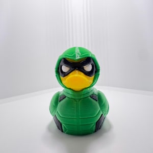 May include: A green and black superhero-themed rubber duck with a yellow beak and white eyes. The duck is wearing a green hood and a green and black costume. The toy is a fun novelty item.