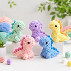 May include: Five colorful, crocheted dinosaur toys in pastel shades of green, purple, yellow, pink, and blue. Each dinosaur has a contrasting color spine and black safety eyes. The toys are arranged on a white surface.