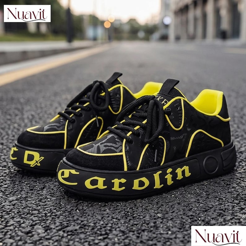 May include: Black and yellow sneakers with the word "Carolin" in yellow on the sole. The sneakers have black laces and a yellow interior. The shoes are on an asphalt surface.