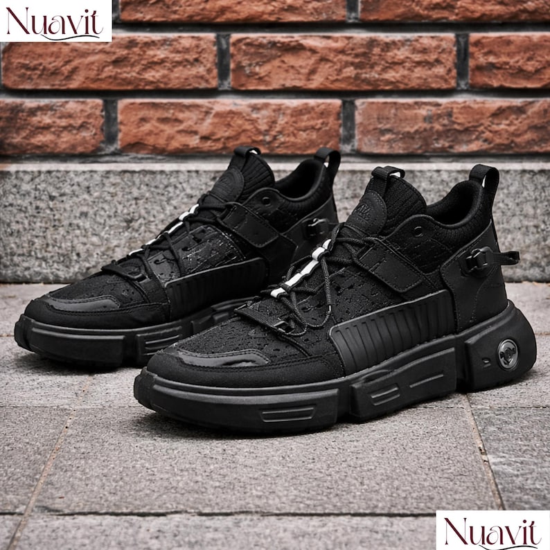 May include: Pair of black sneakers with a chunky sole. The shoes have a textured upper, a lace-up closure with white accents, and a strap across the top. The brand name "Nuavit" is visible in the top left and bottom right corners.