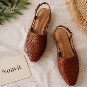 May include: Two brown woven leather slingback flats. The shoes feature a pointed toe and a small heel. The brand name "Nuavit" is visible on the insole. A card with the brand name "Nuavit" is also in the image.