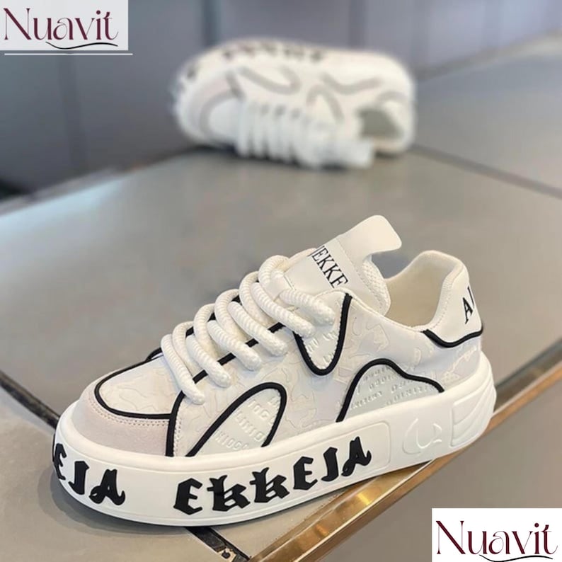 May include: White sneakers with black accents and thick soles. The shoes feature the word "EKKEJA" in bold black letters on the sole and "EKKE" on the tongue. The design includes a textured pattern on the upper.