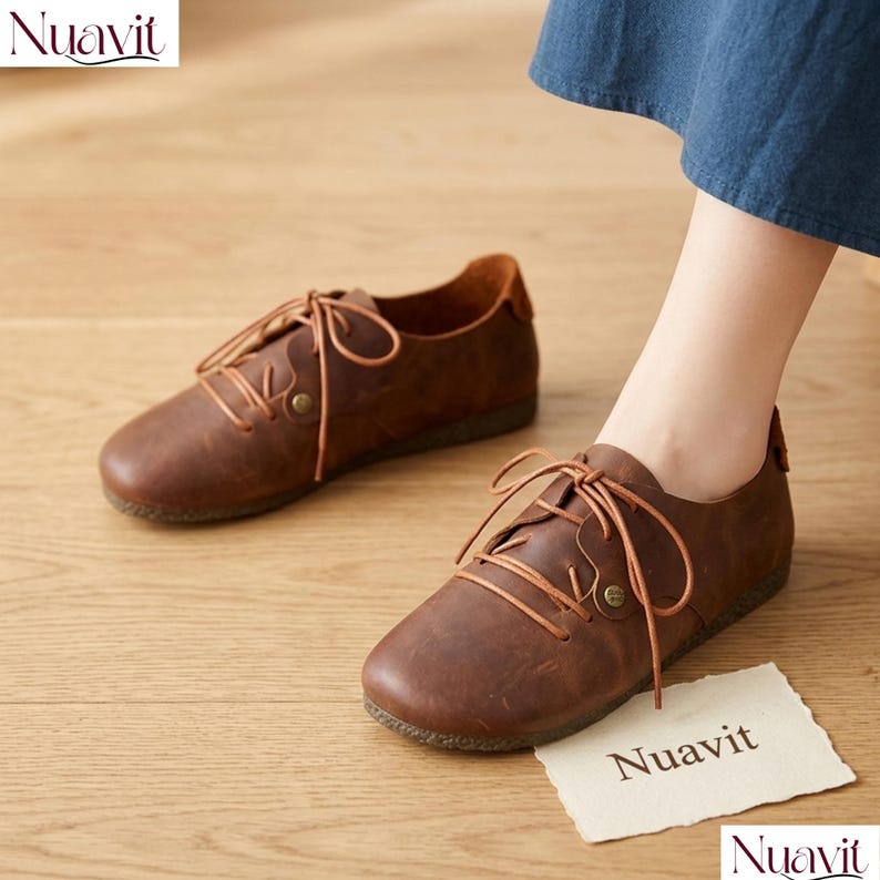 May include: Brown leather lace-up shoes with a rounded toe. The shoes have a classic design with visible stitching and a textured sole. The image includes a piece of paper with the brand name "Nuavit".