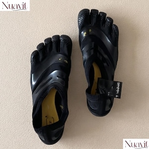 Könnte beinhalten: Ein Paar schwarze Zehenschuhe mit individuellen Zehenfächern, einer flexiblen Sohle und einem gelben Innenfutter. Die Schuhe haben ein schlankes, flaches Design mit schwarzen Überzügen und einem kleinen schwarzen Etikett an der Ferse.