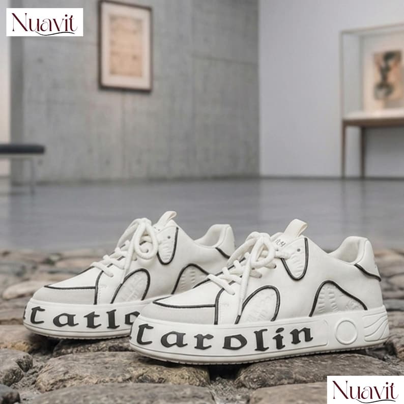 May include: Pair of white sneakers with black trim and the word "Carol&iacute;n" printed on the side. The shoes have white laces and a textured design on the upper. The brand name "Nuavit" is visible in the corner.
