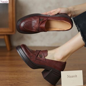 Pode incluir: Mocassins de couro bordô com salto bloco. Os sapatos apresentam um adorno decorativo em forma de rosa na gáspea. A marca "Nuavit" é visível em um pequeno cartão.