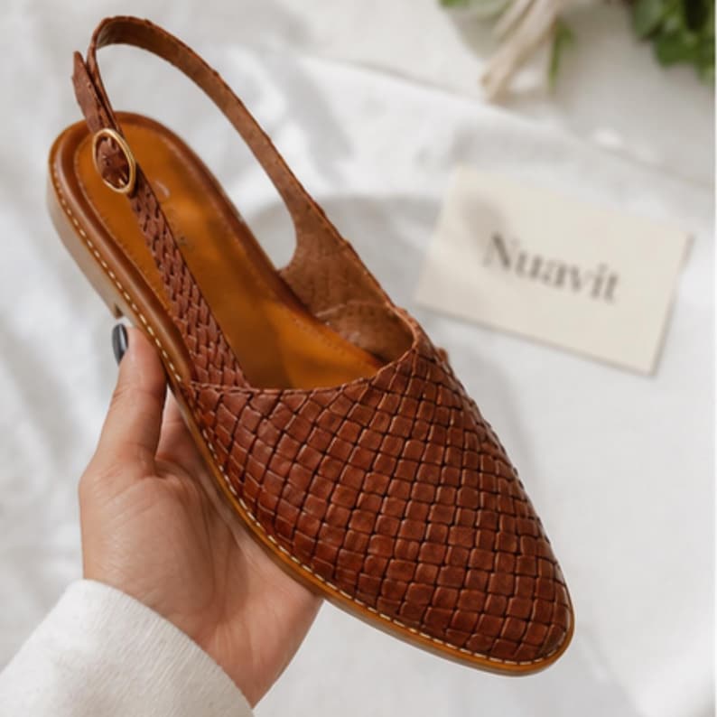 May include: Brown woven leather slingback flats with a pointed toe and adjustable ankle strap. The shoes have a flat sole and a woven pattern across the vamp. The brand name "Nuavit" is visible on a small card.