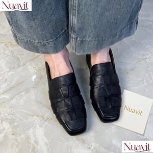以下が含まれることがあります： 黒い革製の編み込みローファー、スクエアトゥ。 靴は下から見え、履いている人の足が見えます。 ブランド名「Nuavit」は左上と小さなカードに表示されています。