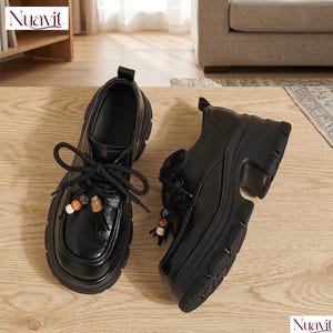 May include: A pair of black platform shoes with thick soles and decorative beaded tassels on the laces. The shoes have a glossy finish and a chunky heel, perfect for a stylish, modern look.