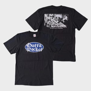 May include: Two black t-shirts. The front shirt has a blue and white oval design with the words "Outta Pocket". The back shirt has a black and white image with text below it. Both shirts have short sleeves.