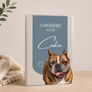 Könnte beinhalten: Eine rechteckige Heimtierausweishülle mit einem blauen vertikalen Feld, das den Text EU-HEIMTIERAUSWEIS 14.02.2020 und den Namen Cookie in weißer Schreibschrift zeigt. Darunter befindet sich eine Illustration einer braun-weißen französischen Bulldogge.