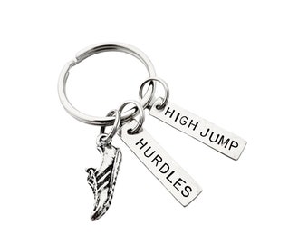 May include: A silver-colored keychain with a running shoe charm and two rectangular tags. The tags read "HURDLES" and "HIGH JUMP". The keychain is on a white background.