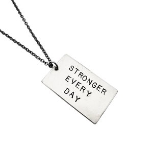 May include: Silver necklace with a rectangular tag that reads "Stronger Every Day".