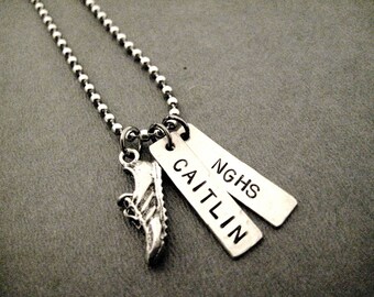 May include: Silver necklace with a silver shoe charm and two silver tags. The tags are engraved with the words "Caitlin" and "NGHS".