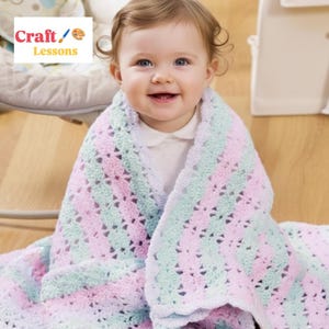 May include: A baby wrapped in a pastel-colored crochet blanket. The blanket features alternating stripes of light pink, mint green, and white. The blanket has a scalloped edge and is wrapped around the baby. The image includes the text "Craft Lessons".