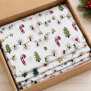 May include: A stack of white tissue paper featuring a repeating holiday pattern of green Christmas trees, red and white candy canes, yellow stars, and colourful string lights, all neatly folded inside a square brown cardboard gift box.