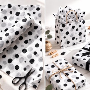 May include: White tissue paper featuring a repeating pattern of black and grey circular polka dots. The set includes flat sheets, a gift bag with handles, and wrapped boxes tied with black satin ribbon or natural jute twine, alongside scissors.