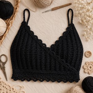 Peut inclure: Un haut court en crochet noir avec un devant croisé, de fines bretelles et un bord festonné le long de l'encolure et de l'ourlet. Le vêtement est réalisé avec un motif de points côtelés verticaux et présenté avec du fil et des outils.