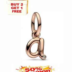 Puede incluir: Charm de oro rosa con forma de la letra minúscula "a" con un pequeño acento de diamante. El charm tiene un lazo en la parte superior para sujetarlo a una pulsera o collar. La imagen también incluye una caja de regalo y un cupón.