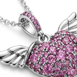 May include: A silver-toned necklace with a heart-shaped pendant. The pendant is encrusted with pink gemstones and features wing-like details. The chain is delicate and the pendant is in focus.
