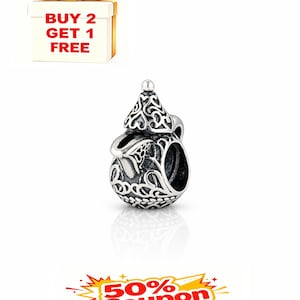 Pode incluir: Um berloque de prata com um design ornamentado e vazado. O berloque tem um corpo arredondado com um topo decorativo e uma argola para prender a uma pulseira ou colar. A imagem também inclui uma caixa de presente e um cupom.