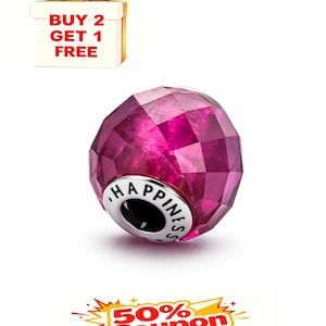 May include: A faceted, magenta-colored bead with the word "HAPPINESS" engraved on a silver-colored band. The bead has a geometric design and is set against a white background. A gift box with a gold bow and the text "BUY 2 GET 1 FREE" is in the background.