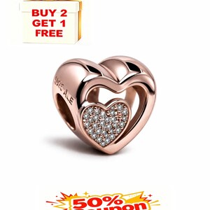 May include: Rose gold heart-shaped charm with a smaller, diamond-studded heart inside. The charm is engraved with "S925 ALE". A gift box with a gold bow and the text "BUY 2 GET 1 FREE" is in the background. A coupon graphic is also present.