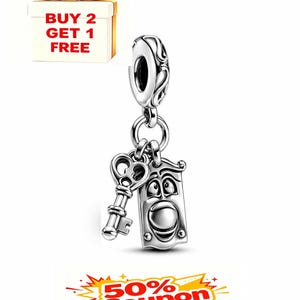 May include: A silver charm featuring a key and a door knocker design. The door knocker has a face with a smiling expression. The charm is suspended from a decorative loop. A gift box with the text "BUY 2 GET 1 FREE" is in the background.