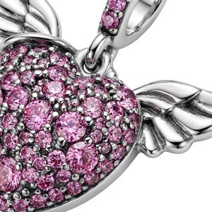 May include: A close-up of a silver charm with a heart shape, covered in pink gemstones. The heart has small, detailed wings on either side. The charm is designed for a bracelet or necklace.