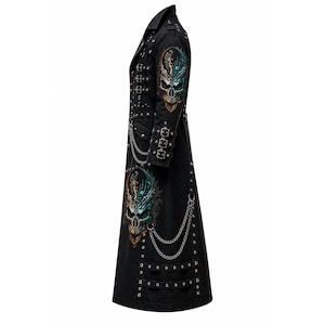 May include: A black long coat featuring a high collar, multiple silver-toned buckles on the chest and sleeves, and silver metal chains. The coat displays colorful skull graphics on the shoulder and lower side, accented with silver studs and grommets.