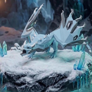 May include: A light blue and gray dragon figurine with a geometric design, posed on a snowy surface. The dragon has open jaws and detailed wings. Blue crystal formations and icicles surround the dragon, creating a fantasy theme.