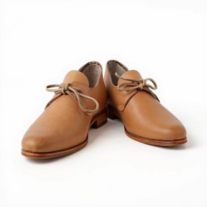 May include: A pair of light brown leather shoes with laces. The shoes have a rounded toe and a low heel. The leather has a smooth texture and a warm, natural color. The laces are tied in a simple bow.