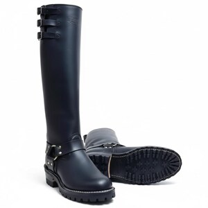 May include: Black leather knee-high boots with three buckles at the top and a harness strap around the ankle. The boots have a lug sole and a stacked heel. One boot is upright, and the other is lying on its side.