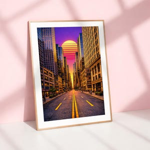 Puede incluir: Impresión artística enmarcada que representa una escena de calle de la ciudad al atardecer. La obra presenta edificios altos que bordean una carretera con líneas amarillas, que conducen a una vibrante puesta de sol con tonos naranja, rosa y morado. El marco es dorado.