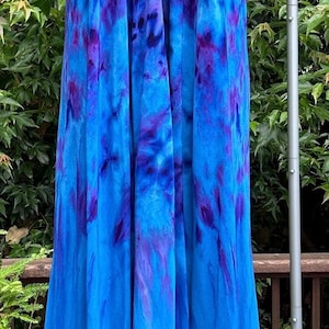May include: A long, halter-neck dress in shades of blue and purple, displayed on a mannequin. The dress features a tie-dye pattern with a flowing, floor-length design. The fabric appears lightweight and suitable for warm weather.