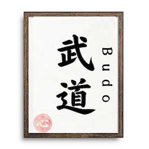 以下が含まれることがあります： 「武道」の漢字が黒インクで描かれた額入りのプリント。 「Budo」という言葉も英語で縦書きされています。 小さな円形の赤いスタンプが左下にあります。 フレームは濃い茶色です。