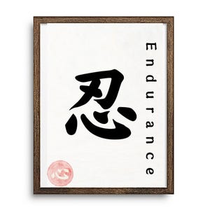 May include: Framed art print featuring a black Japanese Kanji symbol and the word "Endurance" in black. A small, round, pink seal is at the bottom left. The artwork is set against a white background and framed in a brown wooden frame.