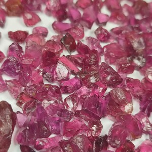 Może przedstawiać: Kolekcja surowych, nieoszlifowanych kamieni szlachetnych rubinu. Kamienie szlachetne różnią się rozmiarem i kształtem, wykazując gamę odcieni różu i czerwieni. Widoczna jest szorstka faktura i naturalne formy kamieni.