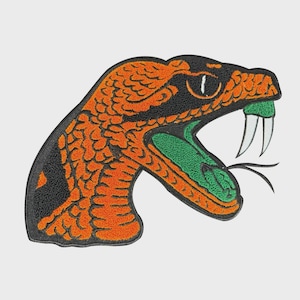 May include: An embroidered patch featuring a stylized snake head with an open mouth. The snake has orange scales, a black head, a green mouth, and white fangs. The patch is likely for clothing or accessories.