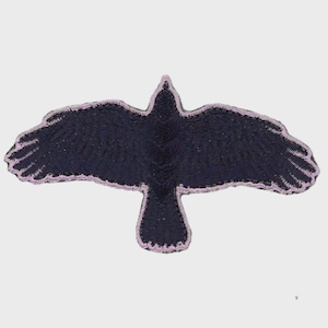 May include: Embroidered patch featuring a black crow in flight with outstretched wings. The crow's outline is accented with a light purple border. The patch is designed to be sewn or ironed onto fabric.