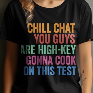 May include: Black t-shirt with the text "CHILL CHAT YOU GUYS ARE HIGH-KEY GONNA COOK ON THIS TEST" in orange, red, green, pink, and blue block letters. The shirt has a crew neck and short sleeves.