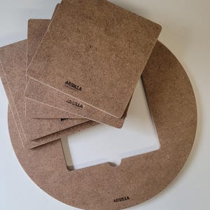 Peut inclure: Ensemble de composants de cadre photo en bois. L'image montre un cadre circulaire avec une ouverture carrée, ainsi que plusieurs inserts carrés en bois. Le mot "ARGILLA" est imprimé sur les pièces en bois.