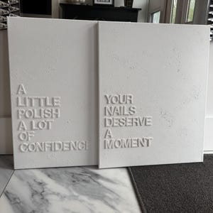 May include: Two rectangular white canvas wall art pieces with raised white lettering. The left canvas reads A LITTLE POLISH A LOT OF CONFIDENCE. The right canvas reads YOUR NAILS DESERVE A MOMENT. Both canvases feature a textured, matte white finish.