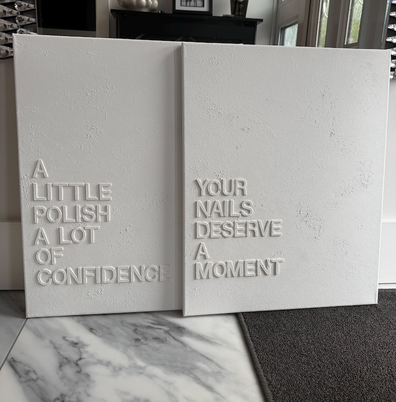 May include: Two rectangular white canvas wall art pieces with raised white lettering. The left canvas reads A LITTLE POLISH A LOT OF CONFIDENCE. The right canvas reads YOUR NAILS DESERVE A MOMENT. Both canvases feature a textured, matte white finish.