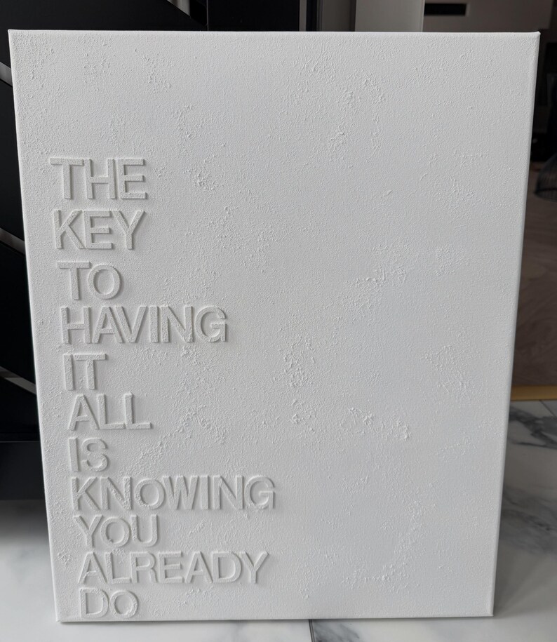 May include: A rectangular white canvas wall art piece featuring a textured surface and raised white lettering that reads: THE KEY TO HAVING IT ALL IS KNOWING YOU ALREADY DO. The text is arranged in a vertical column on the left side of the canvas.