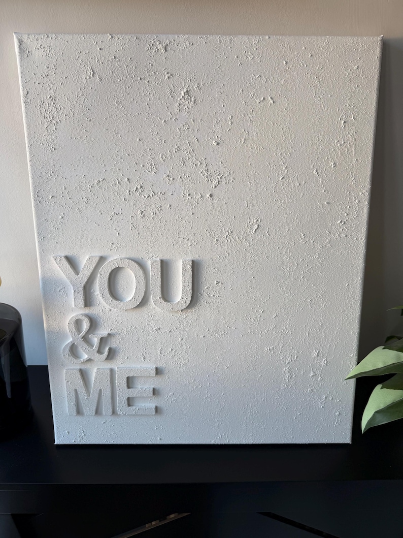 May include: A rectangular white canvas wall art piece featuring a heavily textured, impasto-style surface. The words YOU & ME are displayed in raised, three-dimensional white lettering on the left side of the canvas, creating a monochromatic design.