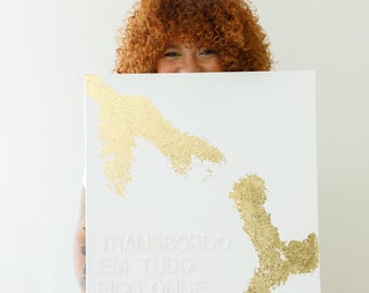 May include: A rectangular white canvas featuring two abstract, textured gold leaf shapes positioned diagonally. Embossed white text reads: TRANSBORDO EM TUDO. FICO ONDE COUBER. The name VANESSA BRUNT is embossed in smaller white letters at the bottom.